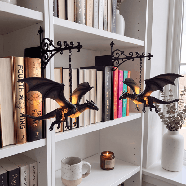 Two Wyrmglow dragon bookends on a white bookshelf with colorful books