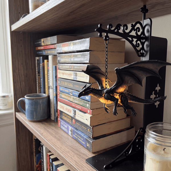 Wyrmglow dragon bookend on a wooden bookshelf with warm amber glow